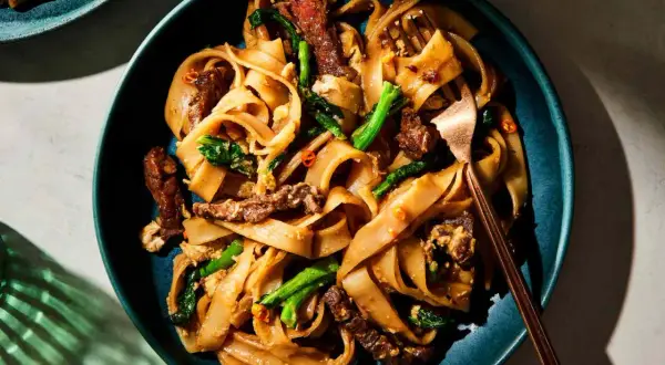 Pad Thai z wołowiną, makaronem ryżowym i zielonymi warzywami na talerzu.
