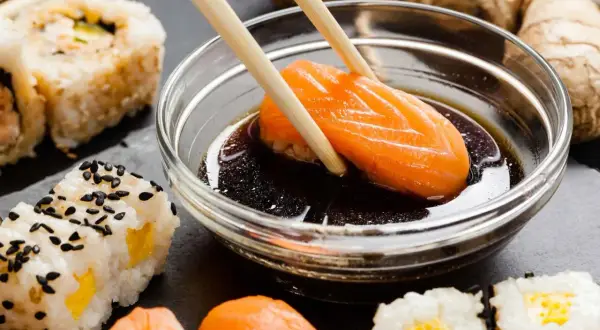 Chopsticks zanurzają kawałek łososia w sosie sojowym do sushi. Obok widać różne rodzaje sushi i imbir.