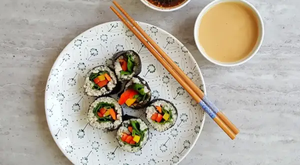 Roladki sushi z warzywami na talerzu, pałeczki i sosy. Tak przygotować nori do sushi, by było pyszne!