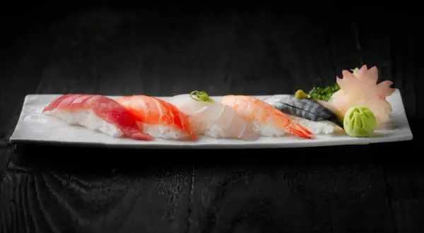 Pięć kawałków sushi z rybą, krewetką i dodatkami na białym talerzu.