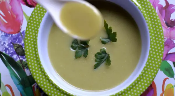 A spoonful of zupa krem z brokułów z ziemniakami, garnished with parsley, sits in a green polka-dot bowl on a floral placemat.