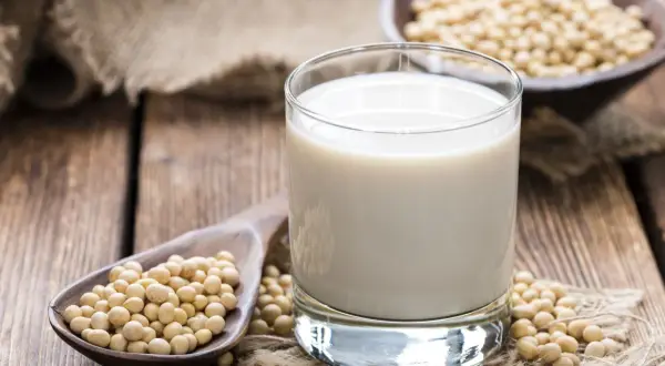 Szklanka mleka sojowego i łyżka ziaren soi. Czy mleko sojowe ma gluten? Nie, jest bezglutenowe.