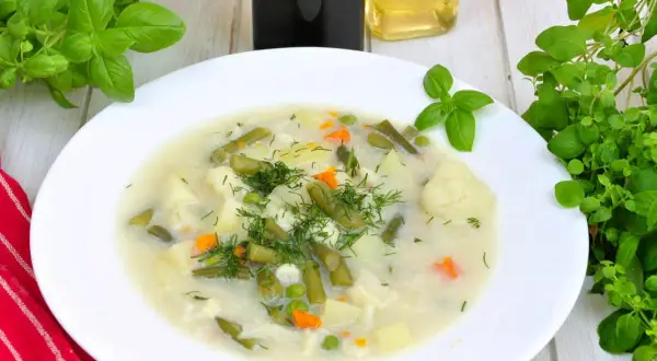 Aromatyczna, tradycyjna zupa jarzynowa z ziemniakami, fasolką szparagową, kalafiorem i groszkiem, udekorowana świeżym koperkiem.