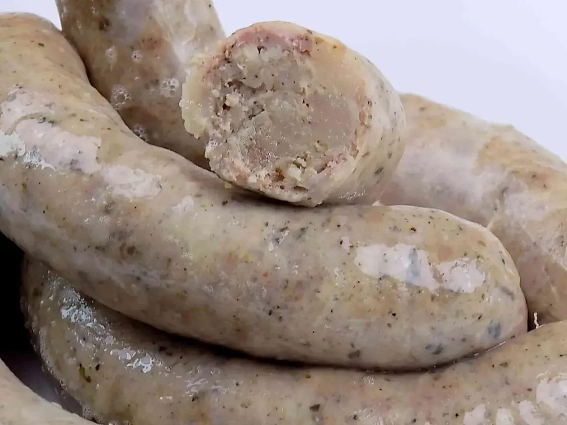 Biała kiełbasa przepis na 3 kg. Gruba, domowa biała kiełbasa, jedna przekrojona, ukazująca wilgotne wnętrze z kawałkami mięsa i przypraw.