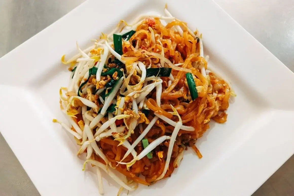 Pad Thai z makaronem ryżowym, kiełkami fasoli mung, jajkiem i szczypiorkiem na białym talerzu.
