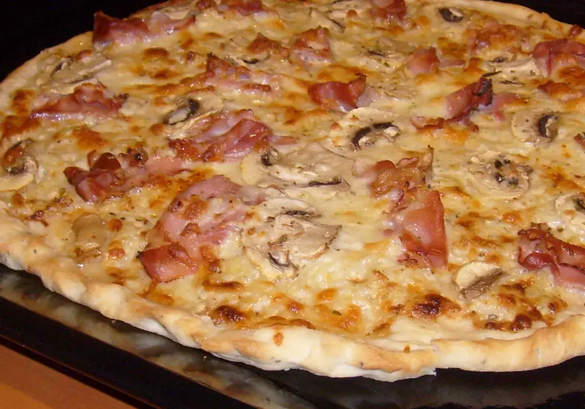 Pyszna pizza carbonara z chrupiącym boczkiem i pieczarkami, obficie posypana serem.