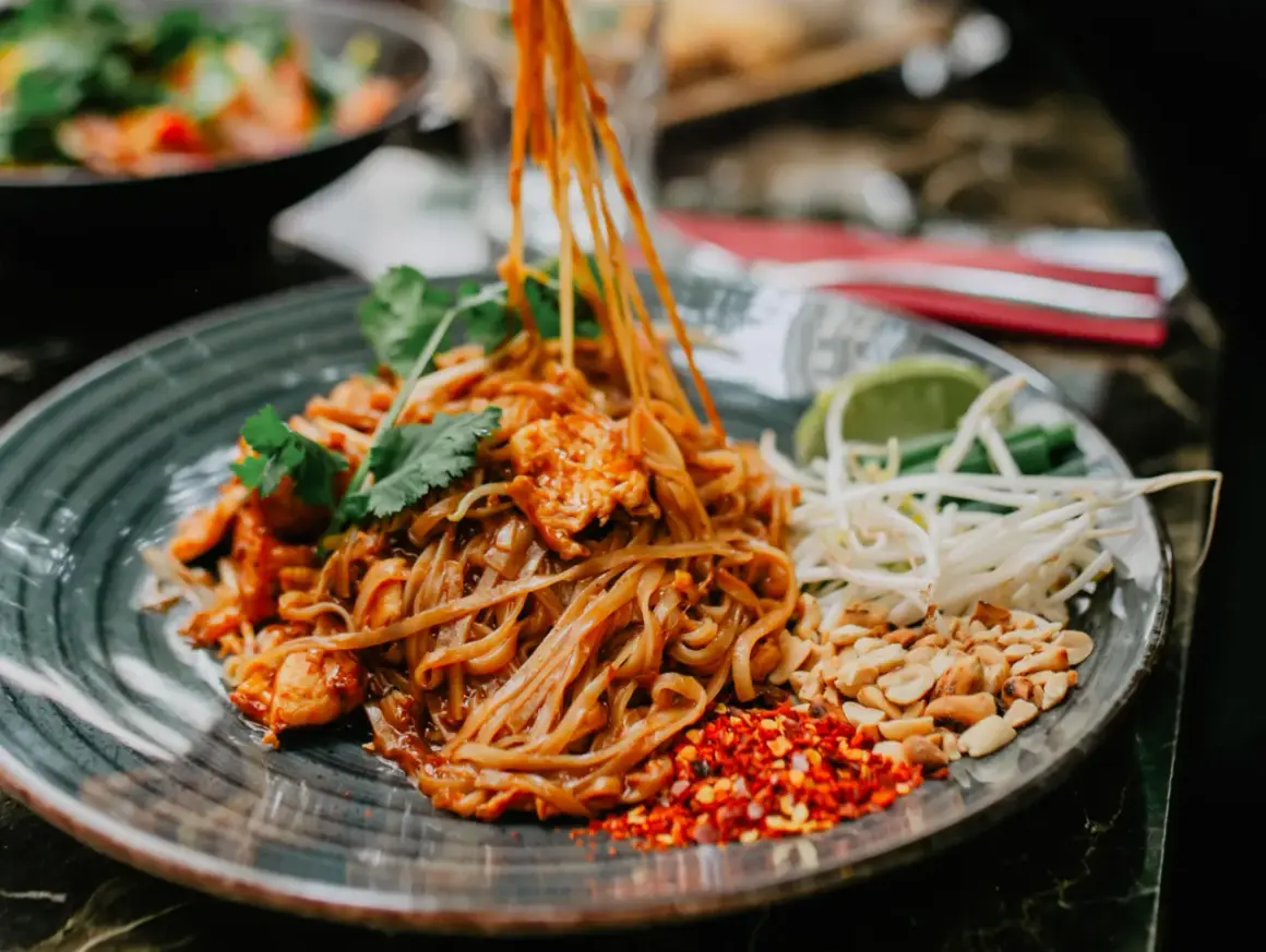 Pyszny pad thai z kurczakiem, orzeszkami, kiełkami i limonką. Tak jemy pad thai, dodając przyprawy do smaku.