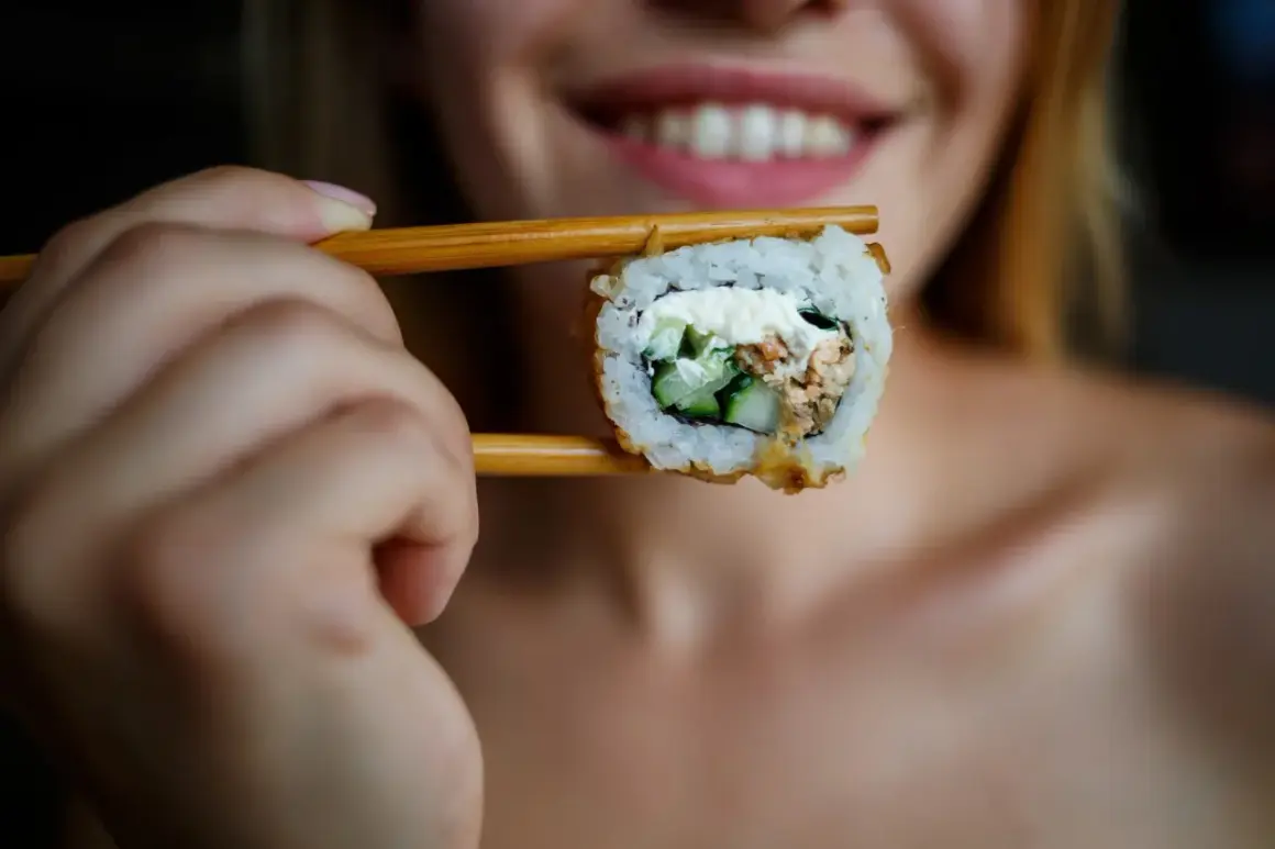 Uśmiechnięta kobieta trzyma pałeczkami sushi, zastanawiając się, czy można jeść sushi karmiąc piersią.