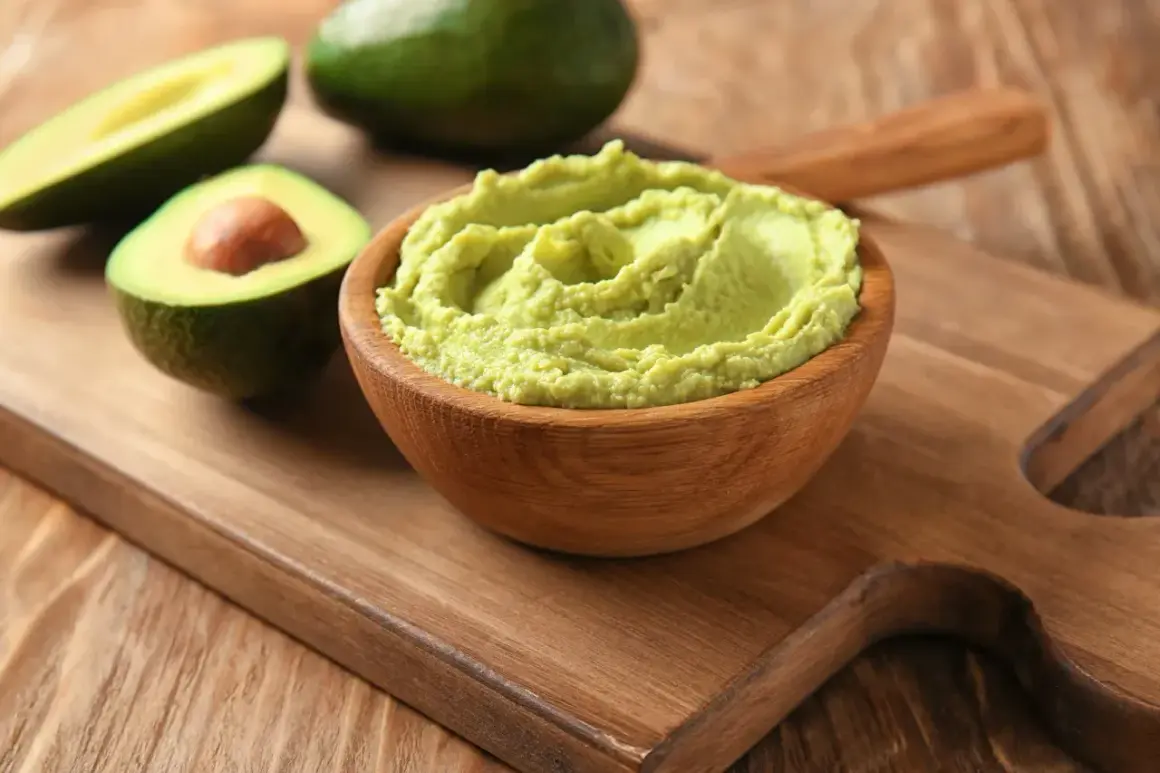 Gotowe guacamole w drewnianej misce, obok przekrojone awokado. Idealne do nauki, jak zrobić guacamole.