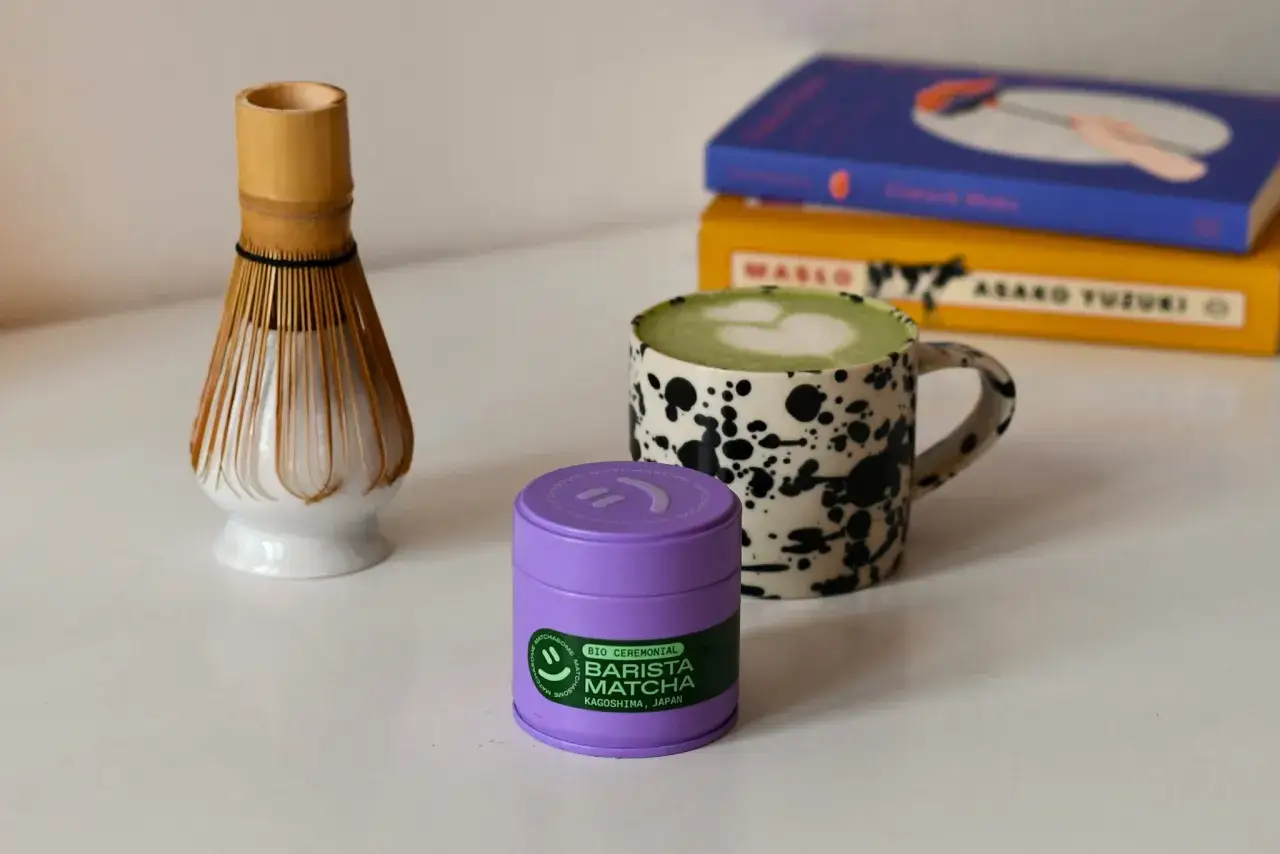 Filiżanka z zielonym matcha latte, bambusowa miotełka do spieniania i fioletowe pudełko z napisem