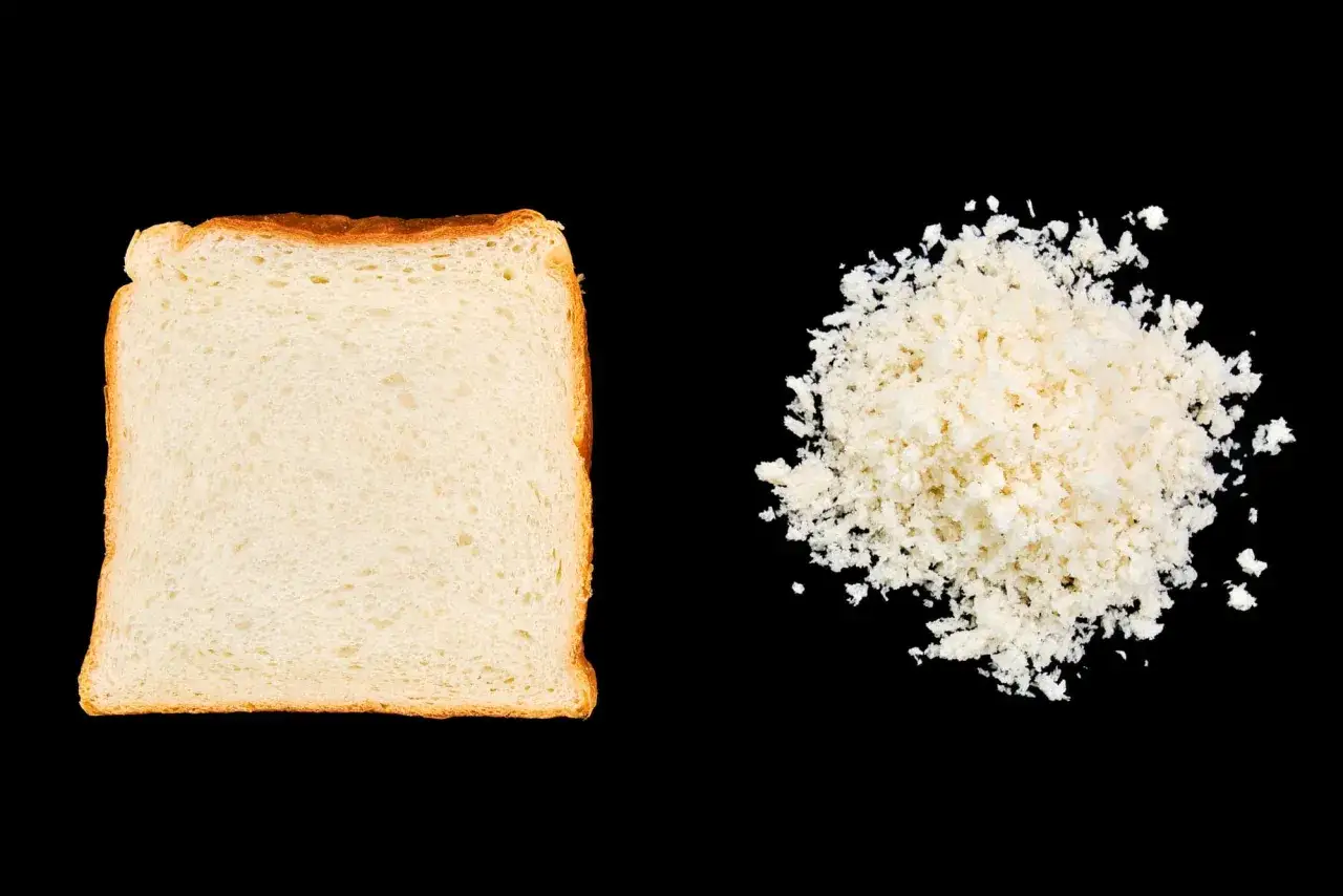 Kromka chleba obok kupki panko. Panko to japońska panierka z pszennego pieczywa, która nadaje potrawom chrupkość.