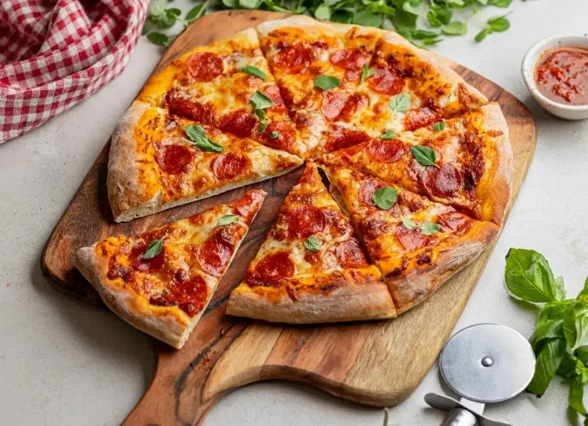 Apetyczna pizza pepperoni z ciągnącym serem i świeżą bazylią, pokrojona na kawałki, gotowa do podania.