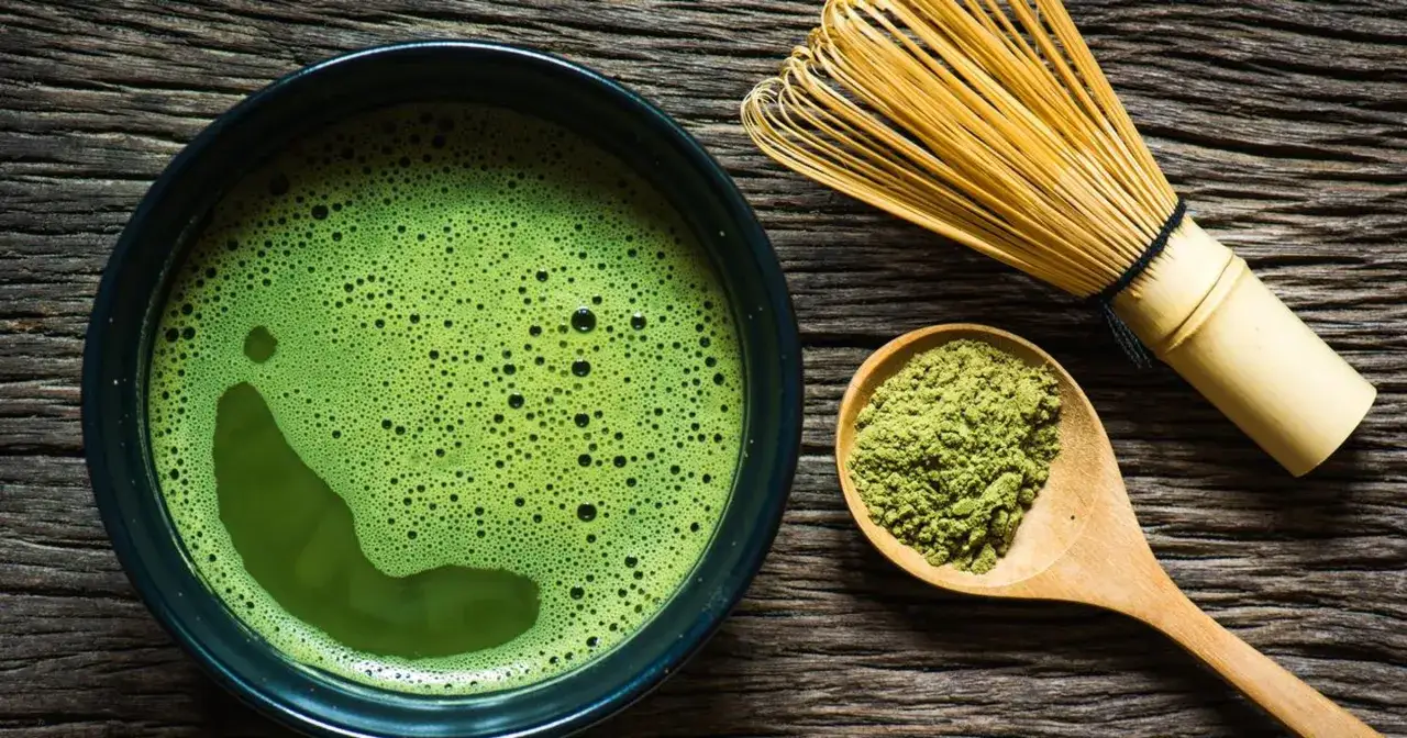 Zielona, spieniona matcha w miseczce, obok bambusowa miotełka i łyżka z proszkiem. To właśnie matcha!