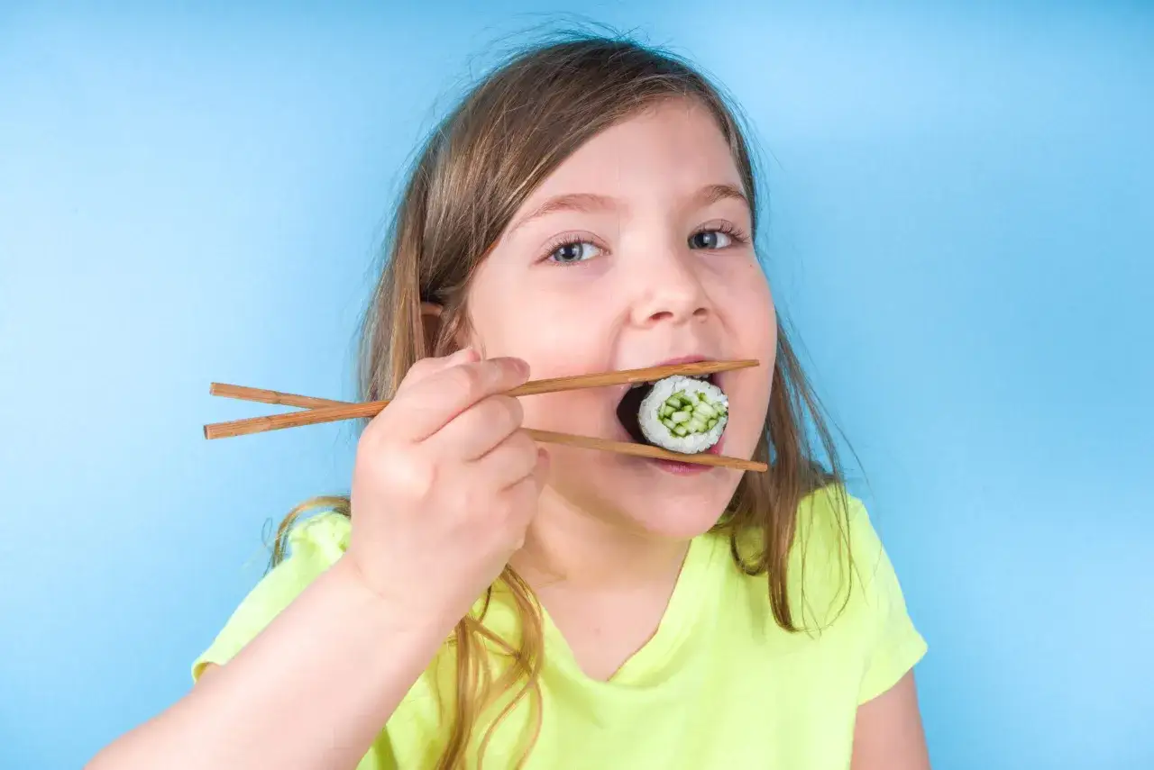 Mała dziewczynka z zapałem próbuje sushi pałeczkami. Czy dzieci mogą jeść sushi? Ta mała miłośniczka kuchni azjatyckiej zdaje się odpowiadać twierdząco!