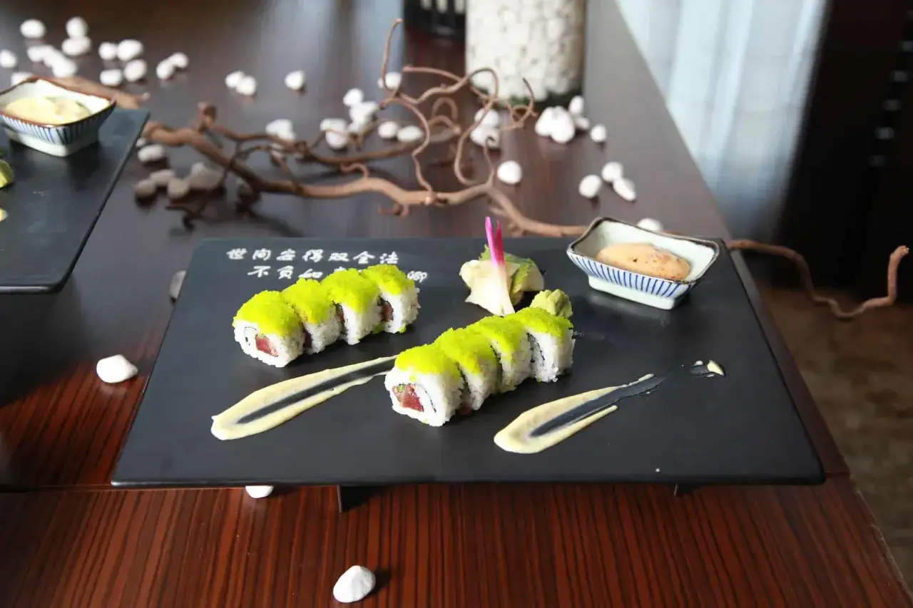 Dwa rzędy sushi z zielonym ikrą, podane z sosem, imbirem i wasabi. Z czym sushi? Z pysznym sosem!