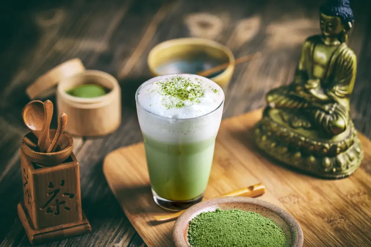 Zielony napój matcha z pianką, obok proszku matcha i bambusowych akcesoriów. Idealny sposób, jak pić matcha dla spokoju.