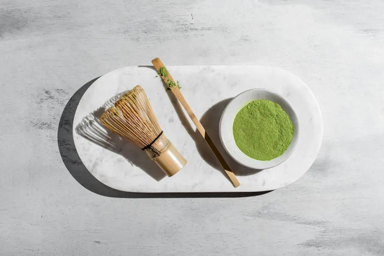 Tradycyjne akcesoria do parzenia matchy: bambusowa miotełka (chasen), bambusowa łyżeczka (chashaku) z proszkiem i miseczka z zielonym proszkiem. Czy matcha pobudza? Zobacz sam!