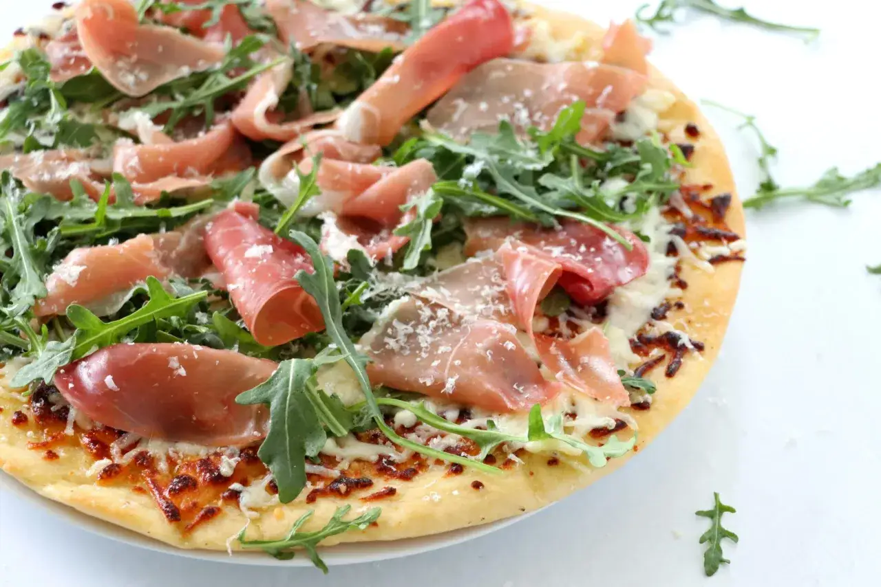 Pyszna pizza prosciutto z rukolą i parmezanem, idealna na szybki obiad.