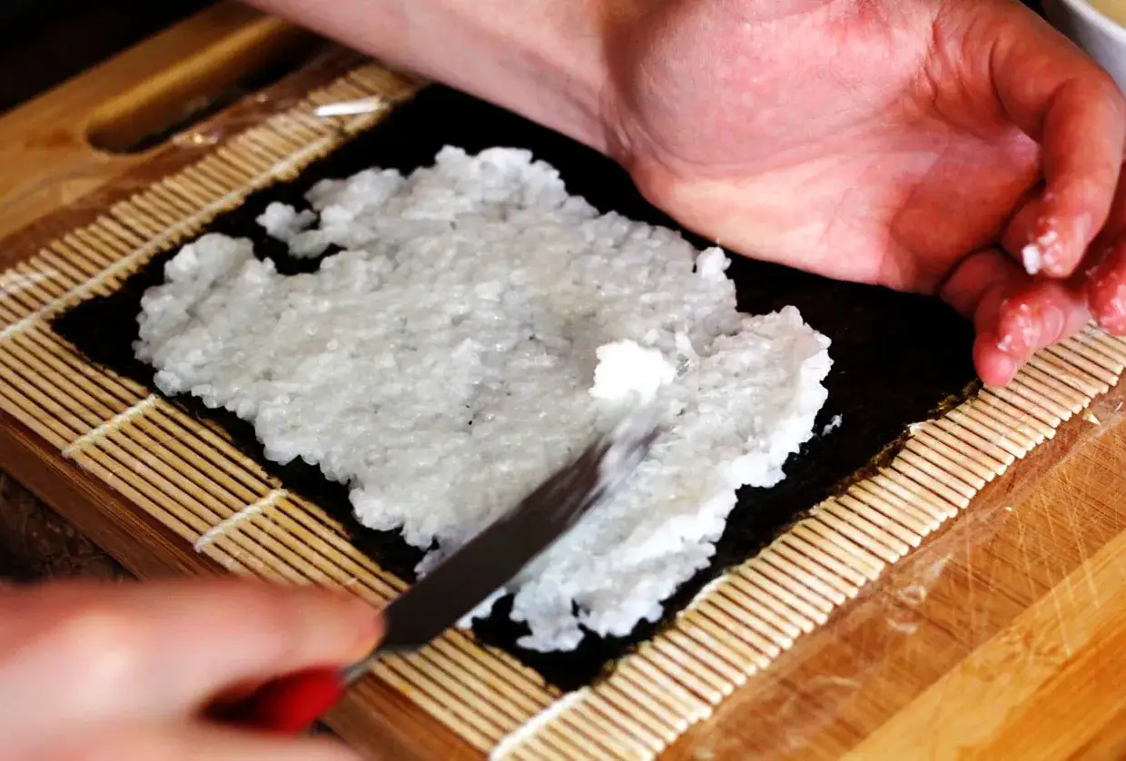 Ręce rozprowadzają ryż na nori, przygotowując się do nauki, jak zawijać sushi.