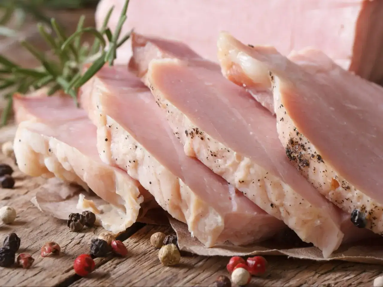 Kawałki super delikatnego i soczystego schabu gotowanego, przyprawione pieprzem, z gałązką rozmarynu na drewnianym blacie.