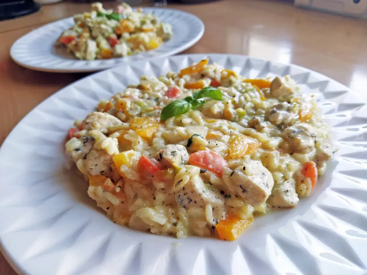 Klasyczne risotto z kurczakiem, z kawałkami papryki i bazylią, podane na białym talerzu.