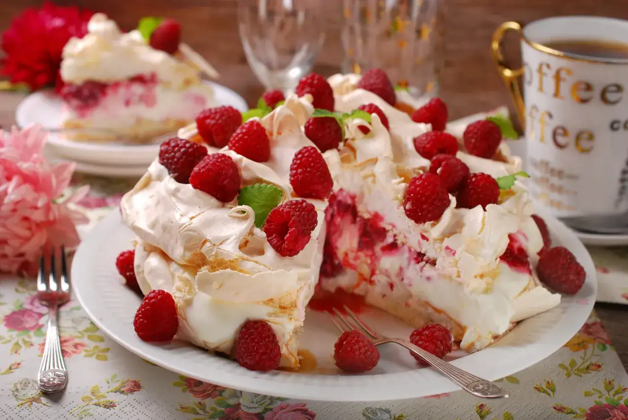 Pyszny tort bezowy z mascarpone i bitą śmietaną, ozdobiony malinami i miętą. Idealny deser na każdą okazję.
