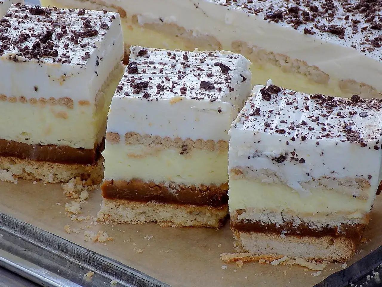 Pyszne ciasto 3 bit bez pieczenia z warstwami kremu, ciastek i karmelu, posypane czekoladą.