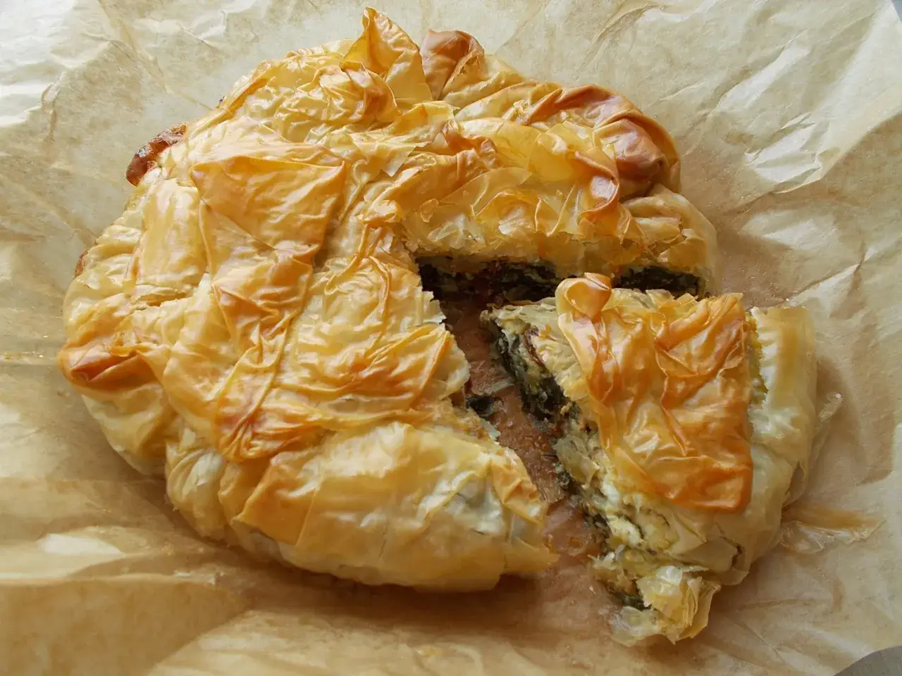 Złocista, chrupiąca spanakopita z widocznym nadzieniem ze szpinaku i sera feta, ułożona na papierze do pieczenia.