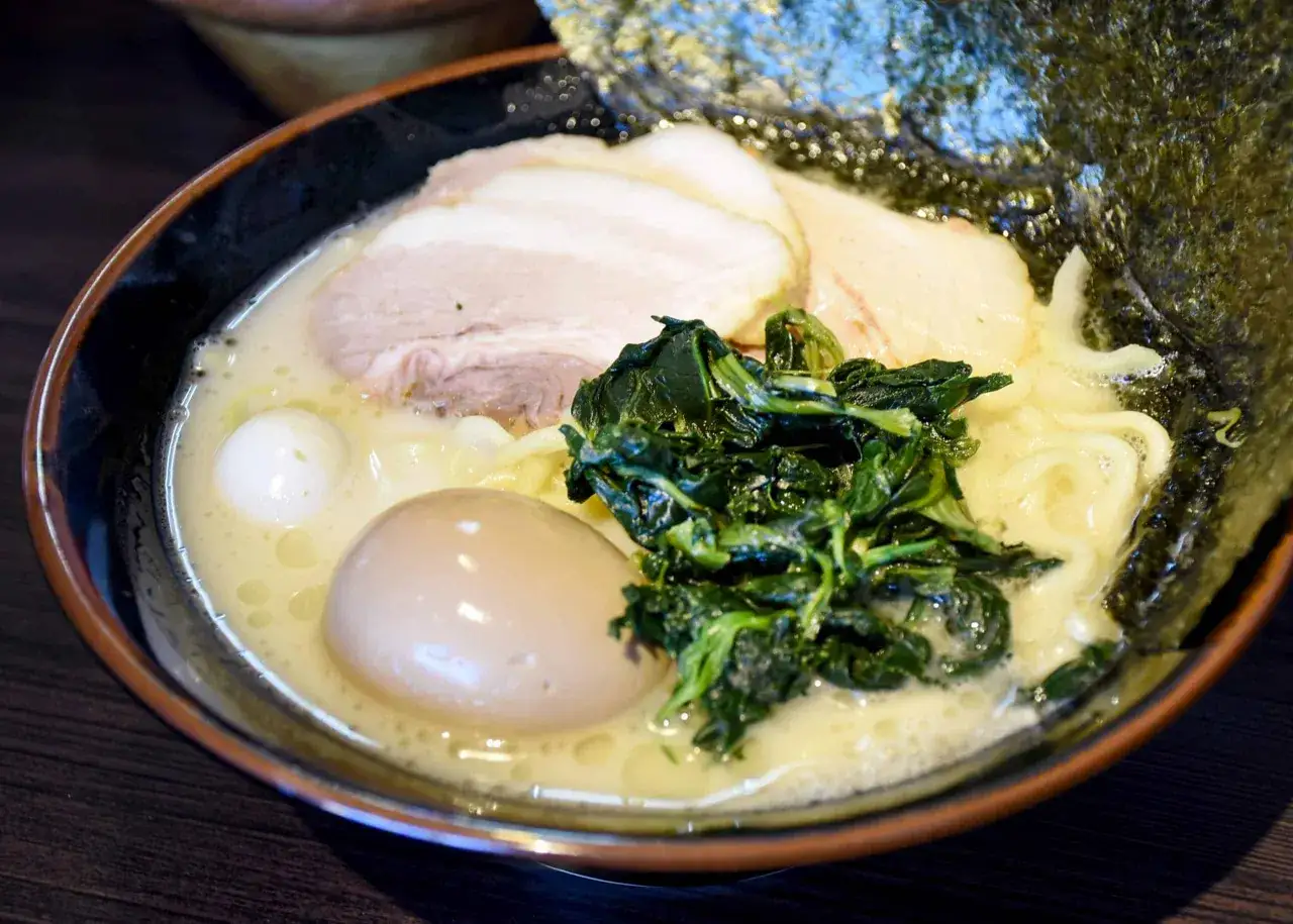 Miseczka ramenu z makaronem, plastrami wieprzowiny, zielonymi warzywami i połówką jajka. Idealne jajko do ramen to klucz do sukcesu.