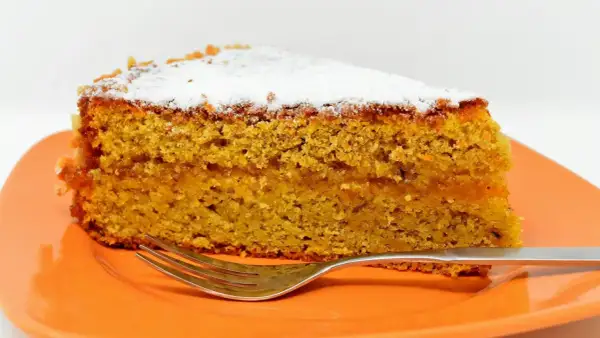 Wilgotne ciasto marchewkowe, posypane cukrem pudrem, idealne jako ciasto dla cukrzyków. Obok leży widelec.