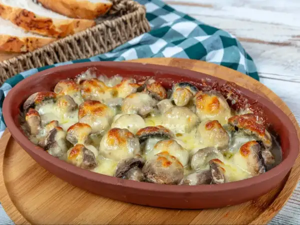 Pyszne pieczarki z piekarnika zapieczone pod ciągnącym serem, podane w glinianym naczyniu. Idealne z chrupiącą bagietką.