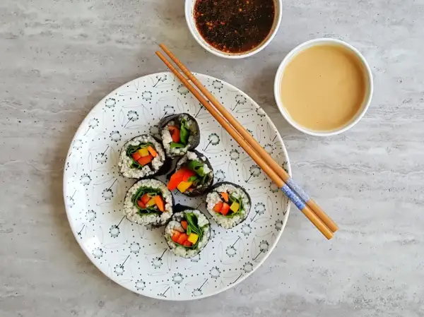 Roladki sushi z warzywami na talerzu, pałeczki i sosy. Tak przygotować nori do sushi, by było pyszne!