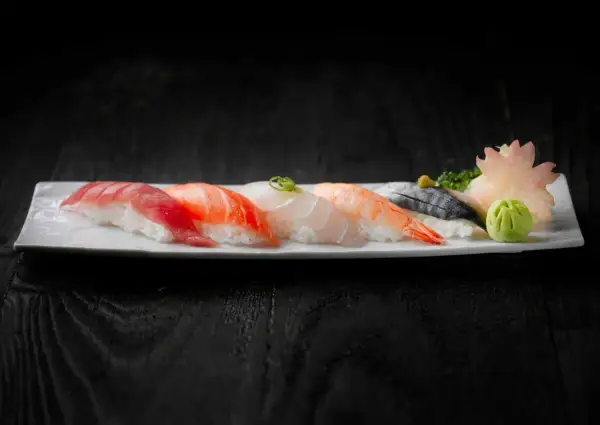 Pięć kawałków sushi z rybą, krewetką i dodatkami na białym talerzu.
