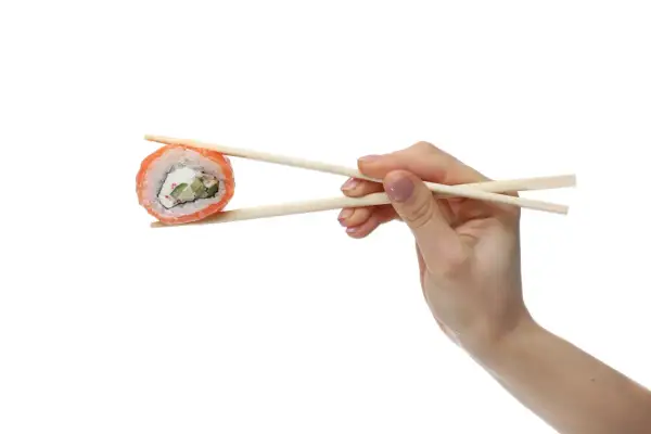 Dłoń trzymająca pałeczkami do sushi kawałek rolki sushi z łososiem i serkiem.