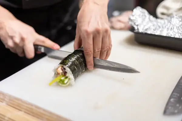 Dłonie kroją rolkę sushi. Zastanawiasz się, czy sushi można zamrozic? Ten obrazek pokazuje przygotowanie świeżego sushi.